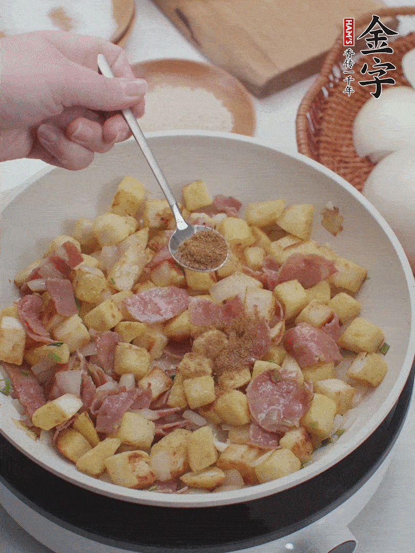 起鍋少油，煸香洋蔥丁、蔥白，加入金字培根火腿翻炒幾下，再加入饅頭丁、1小勺孜然粉、少許鹽翻炒均勻并鋪平。